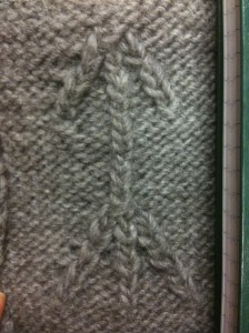 A swatch of knitted fabric showing a cabled arrow pointing upwards.